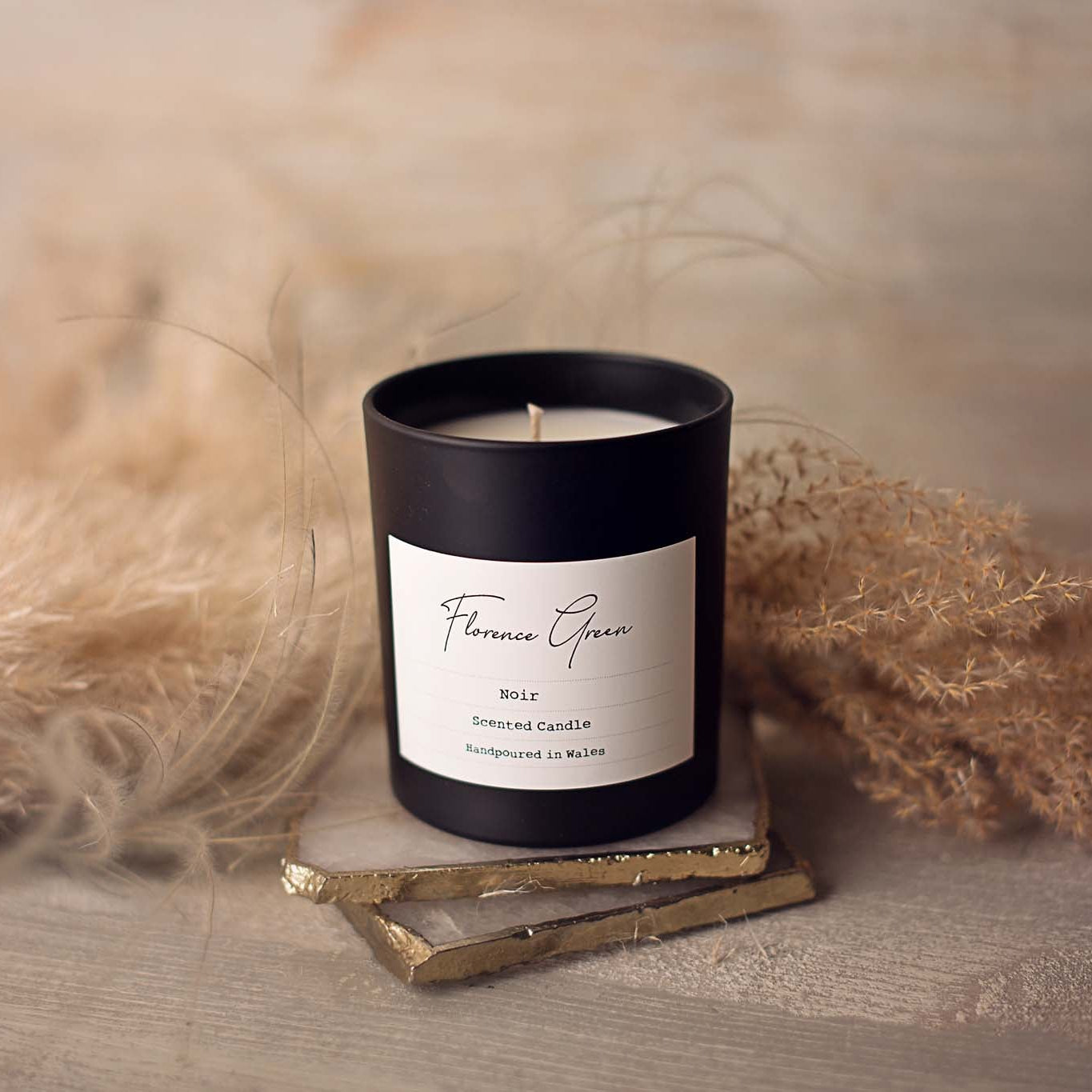 Black candle with a white label on a wooden surface with dried plants