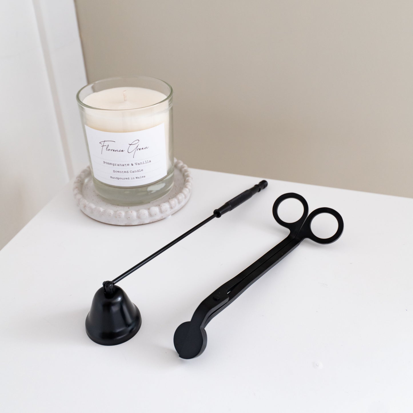 Black candle snuffer and wick trimmer on a white surface with a candle in the background.