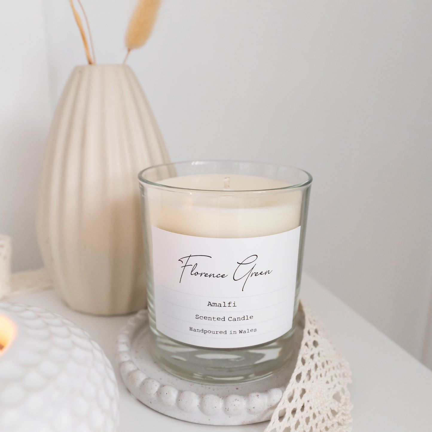 Candle with a label in a decorative setting with a vase and decorative elements.
