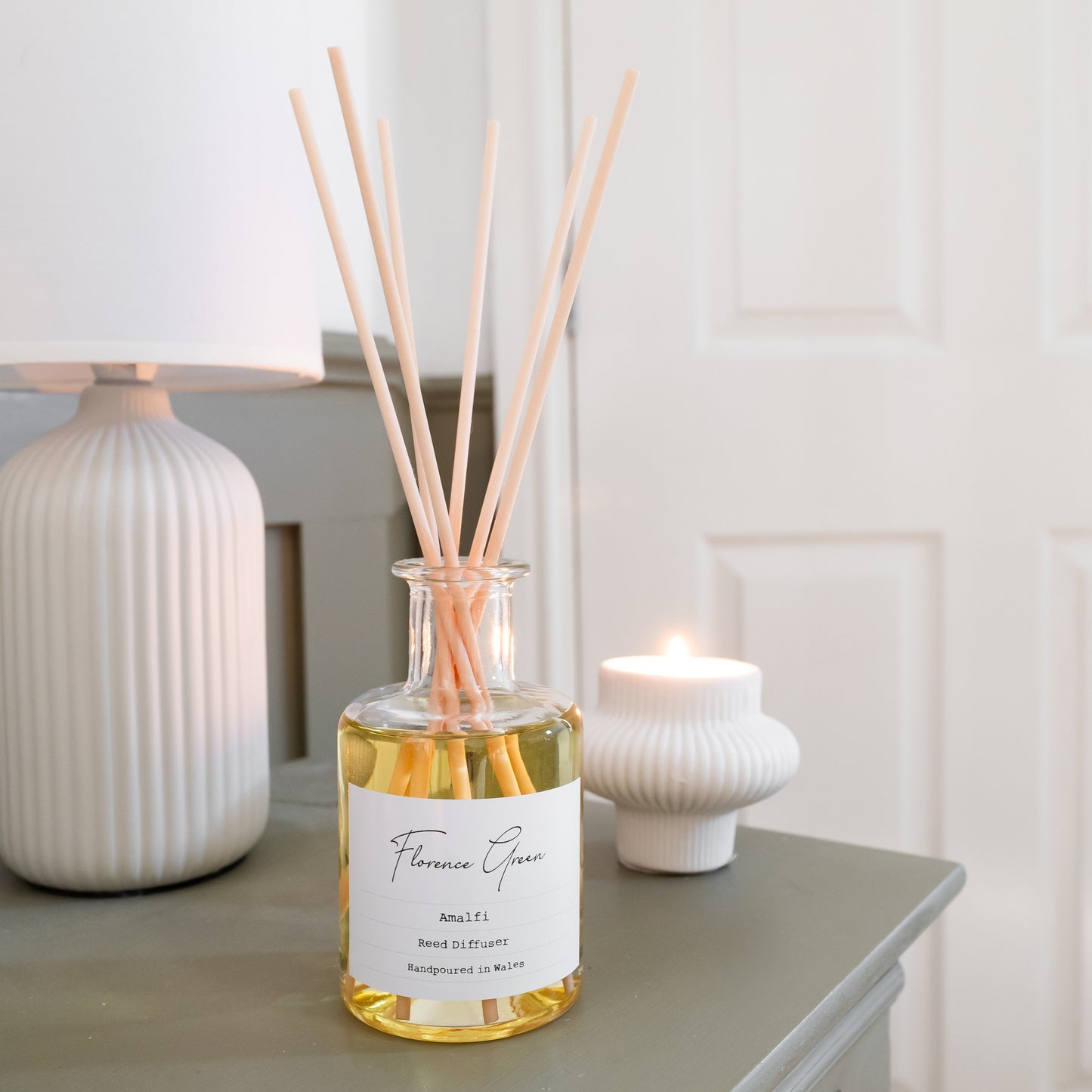 Reed diffuser bottle on a table with a lamp and candle in the background