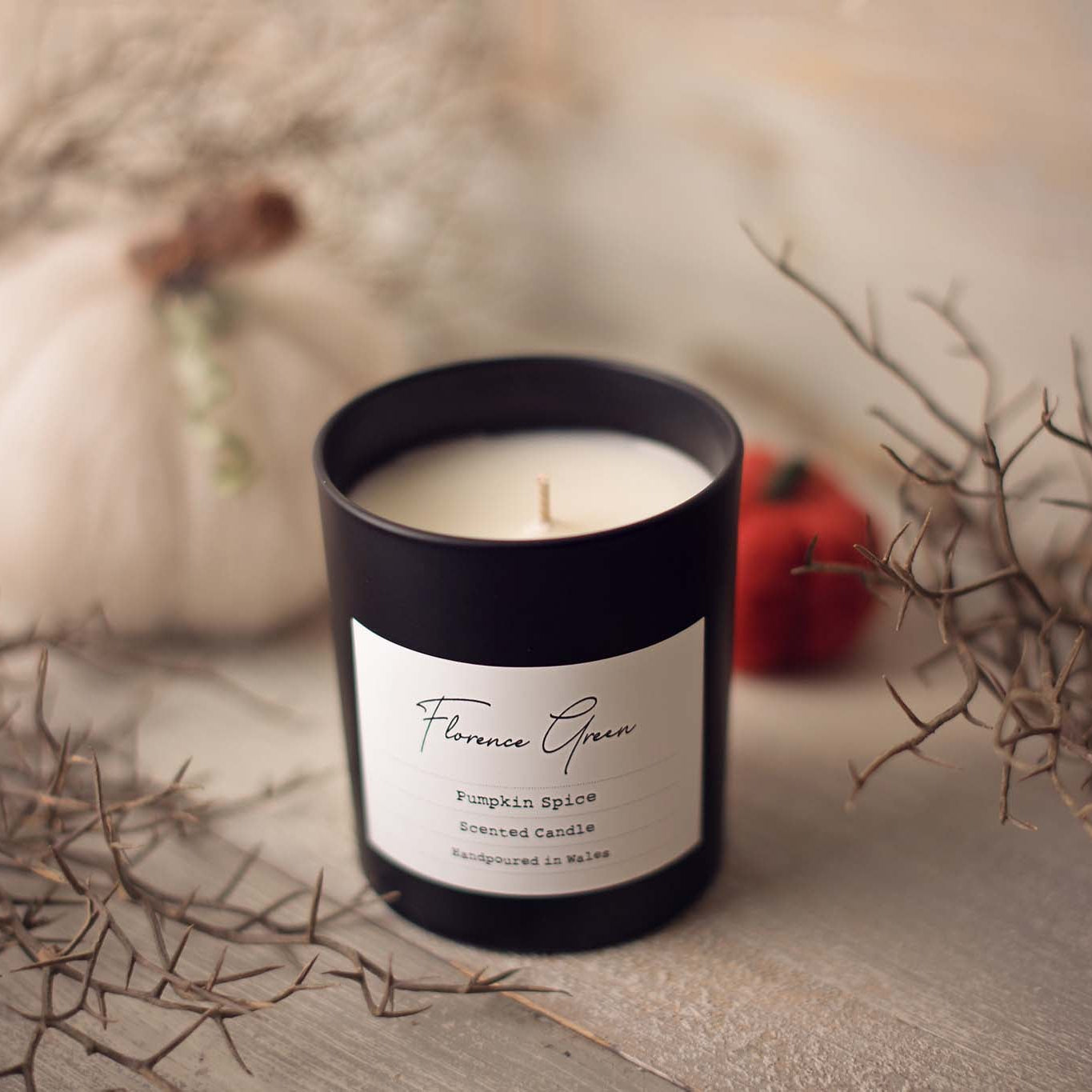 Candle with a label on a surface with pumpkins and branches