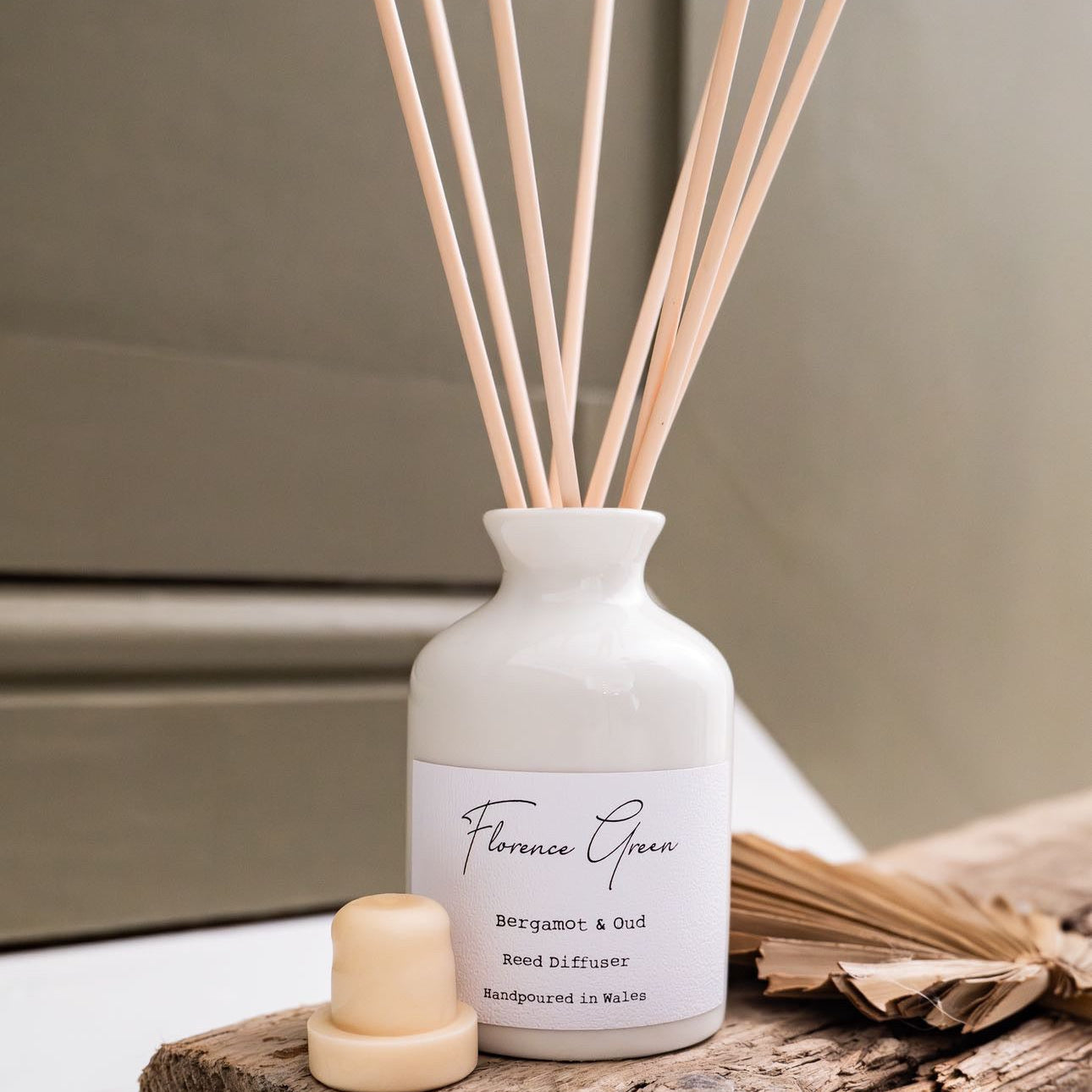 White diffuser bottle with wooden sticks on a wooden block against a neutral background