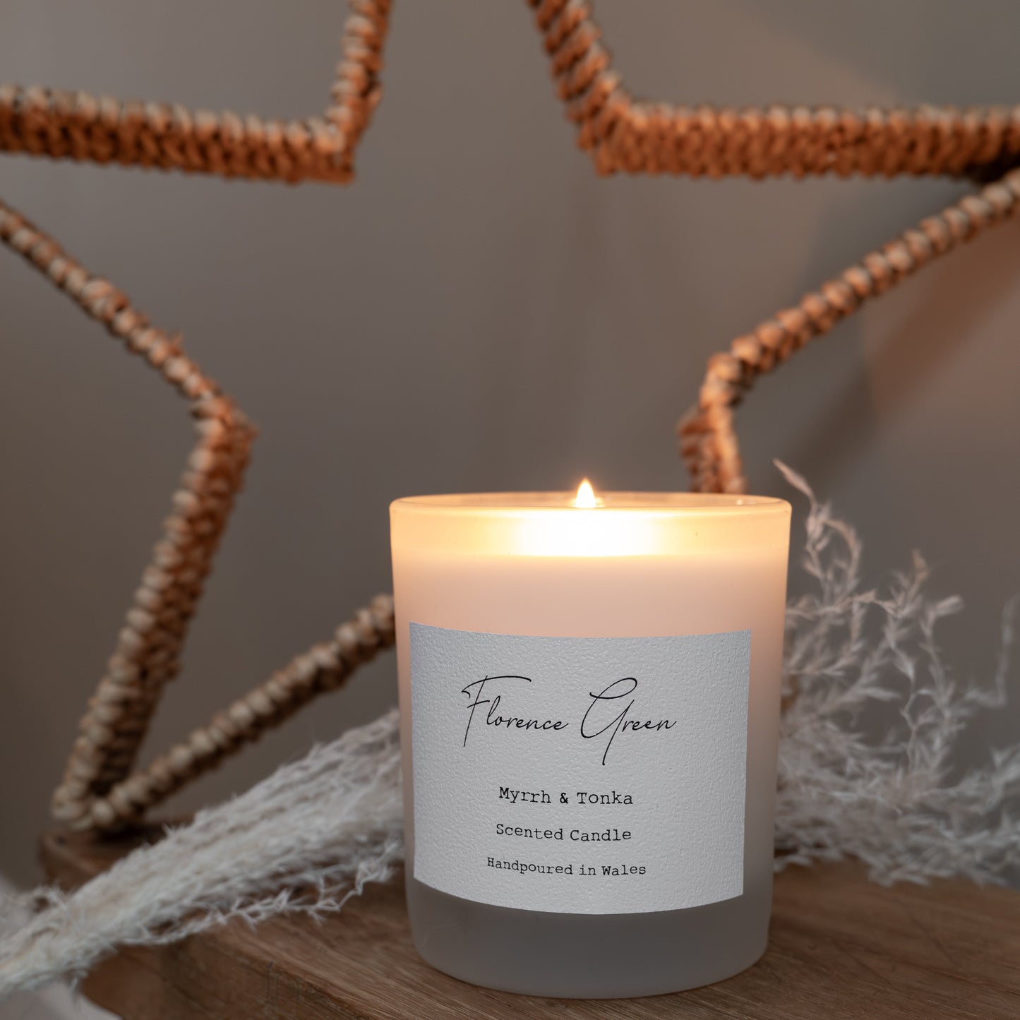 Candle with a label on a wooden surface with a star-shaped candle holder in the background.