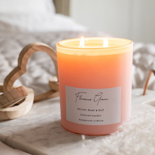 Pink candle with a label on a marble surface, surrounded by soft lighting.
