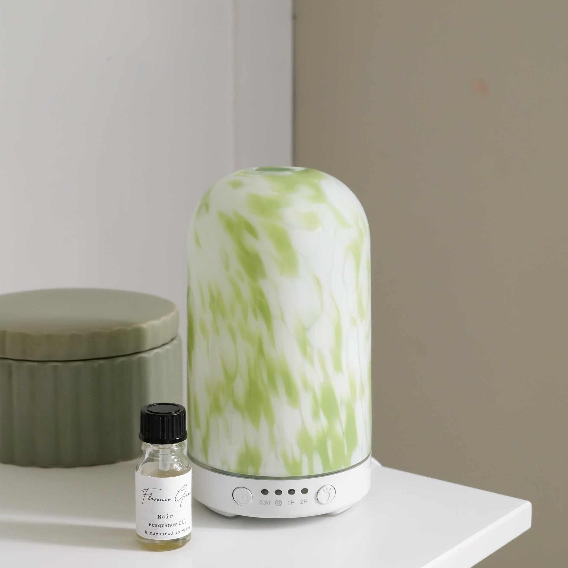 Green and white diffuser on a white surface with a small bottle nearby.