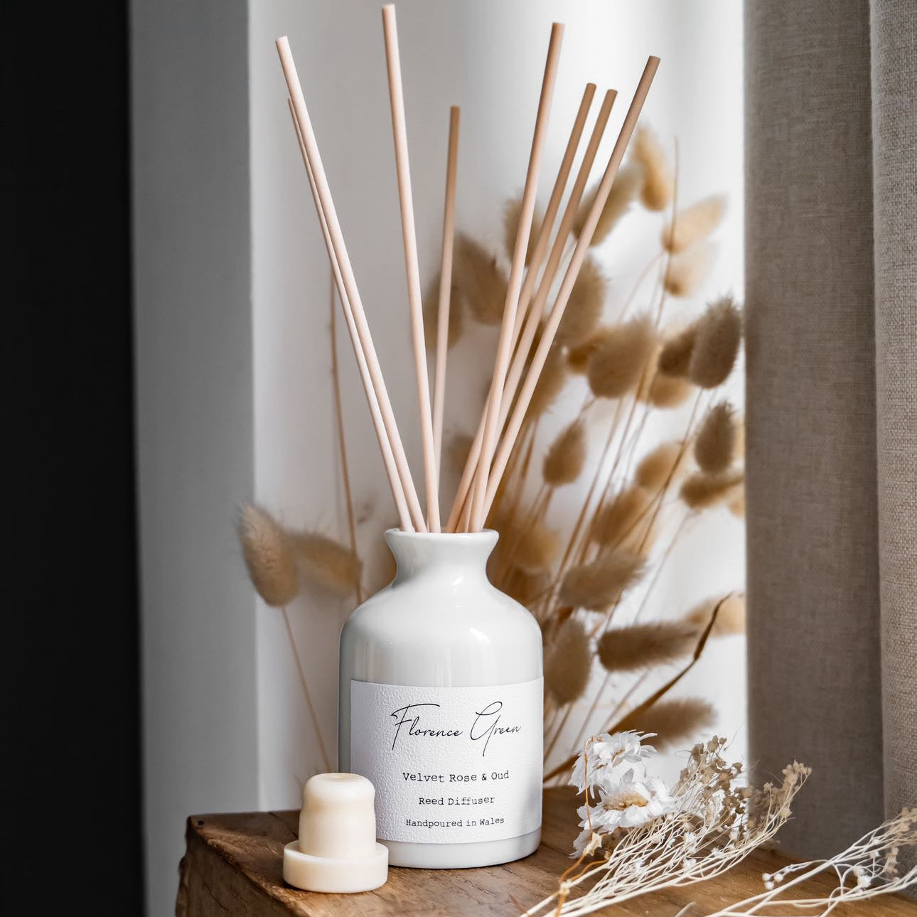 White diffuser bottle with reeds on a wooden surface with dried plants in the background