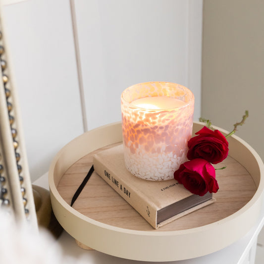 Round wooden tray with a candle, book, and red roses on a white surface.