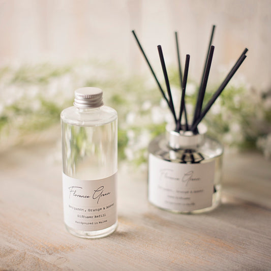 Reed diffuser set with bottle and sticks on a wooden surface with blurred flowers in the background