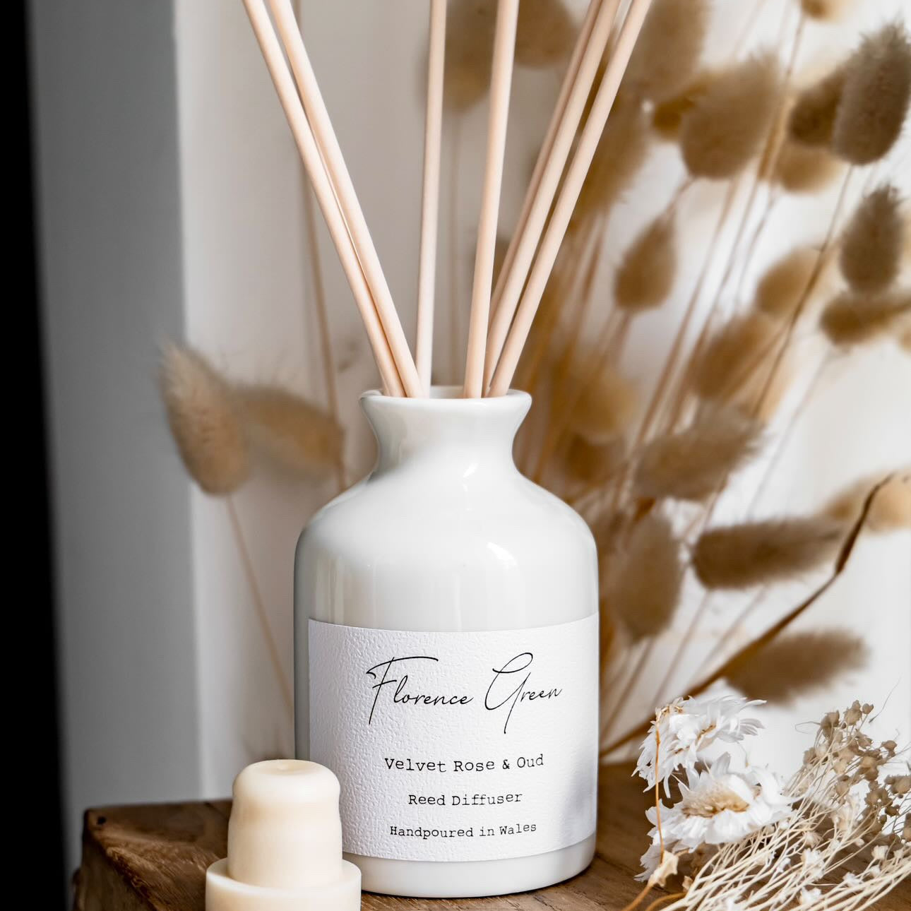 White diffuser bottle with wooden sticks on a wooden surface with dried plants.