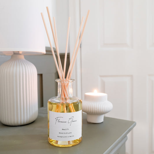 Reed diffuser bottle on a table with a lamp and candle in the background