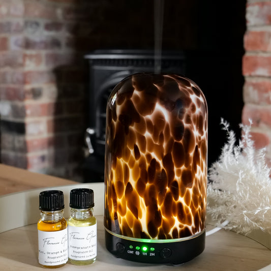 Tortoiseshell-patterned diffuser on a table with two bottles next to it, against a brick wall background.