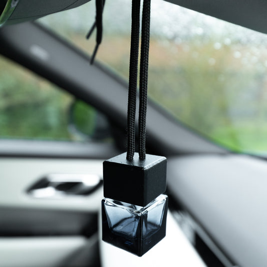 Car air freshener hanging from a car's rearview mirror with a blurred outdoor background