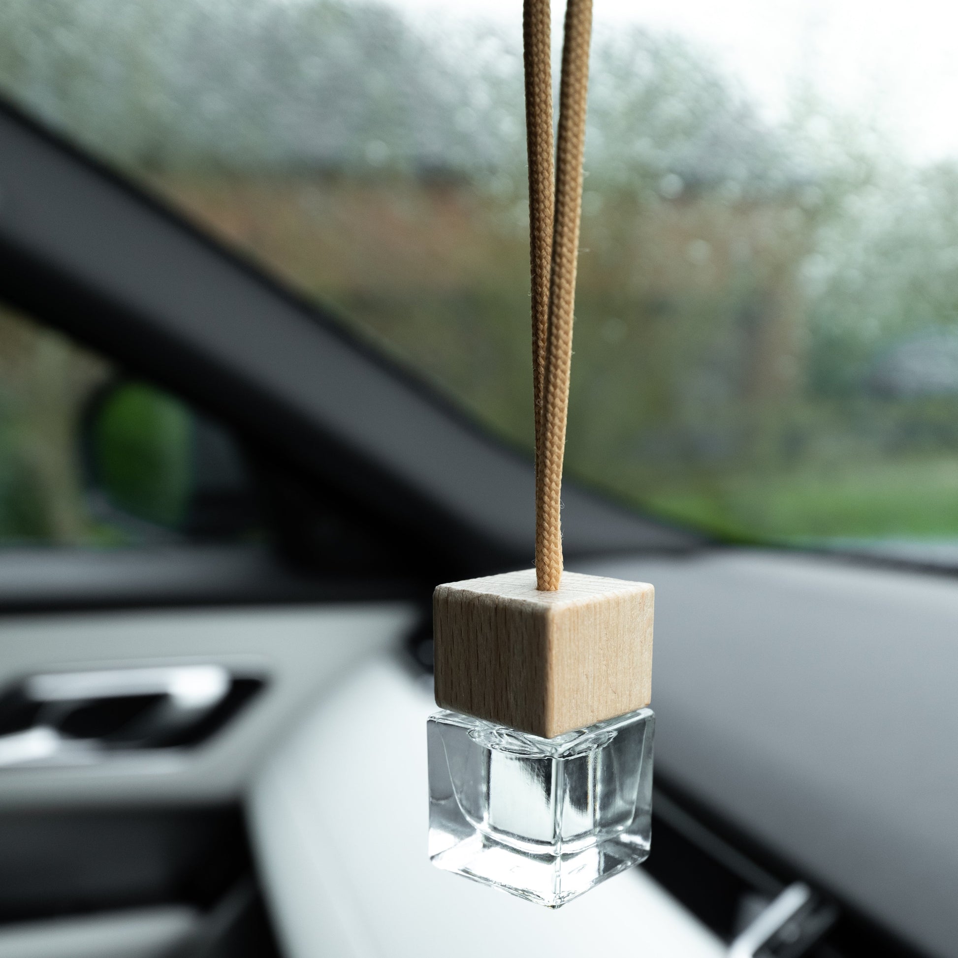 Car air freshener hanging from a car's rearview mirror with a blurred outdoor background.