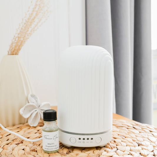 White diffuser on a woven surface with a small bottle of essential oil next to it, against a neutral background.