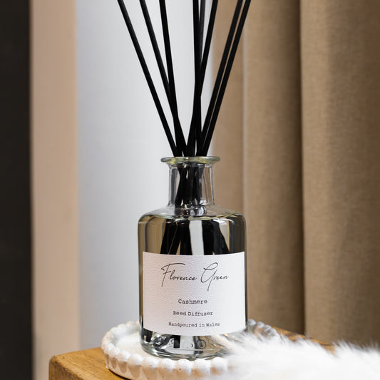 Reed diffuser with black sticks in a clear bottle on a wooden surface.