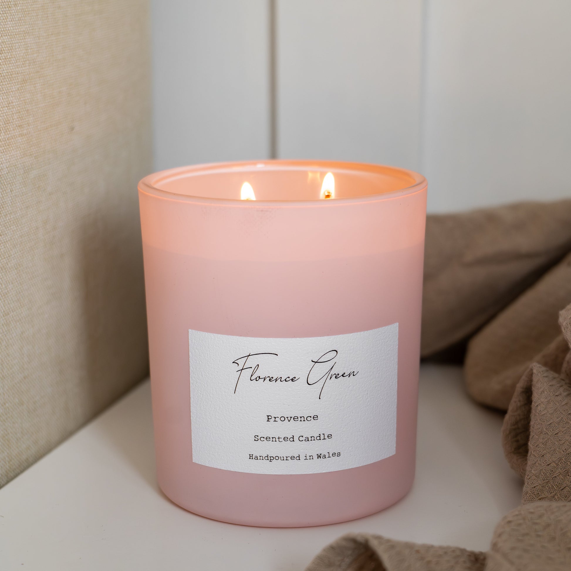 Pink candle with a label on a white surface, with a neutral background