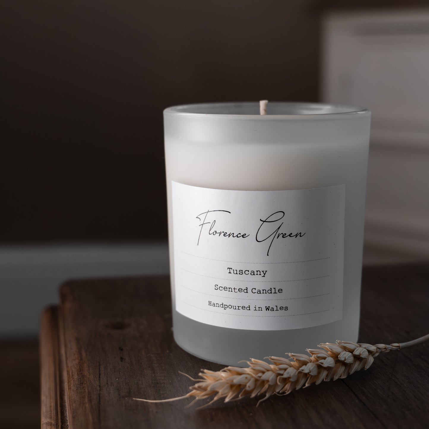 Frosted candle labeled 'Florence Green' on a wooden surface with a blurred background