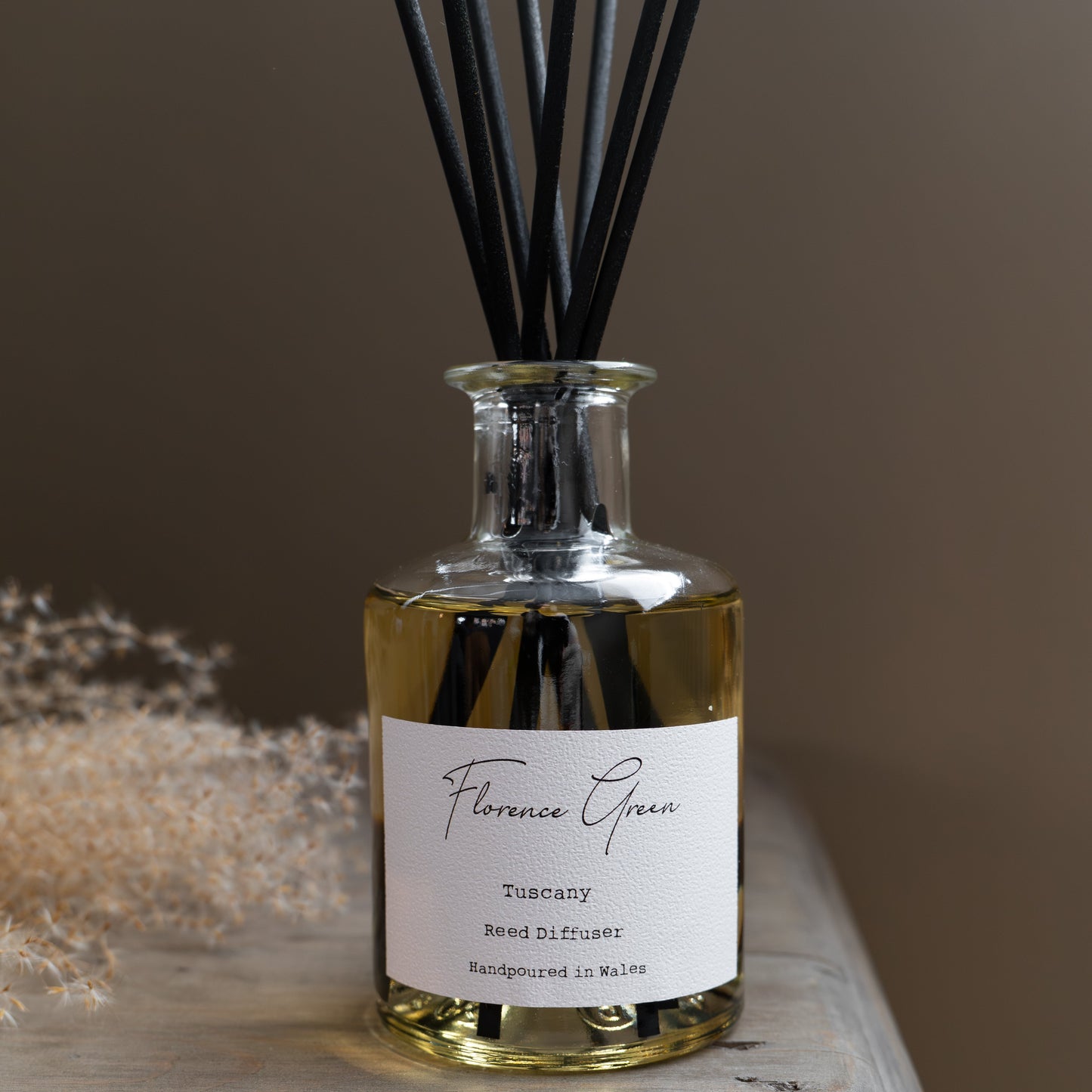 Reed diffuser bottle with black reeds on a wooden surface against a brown background