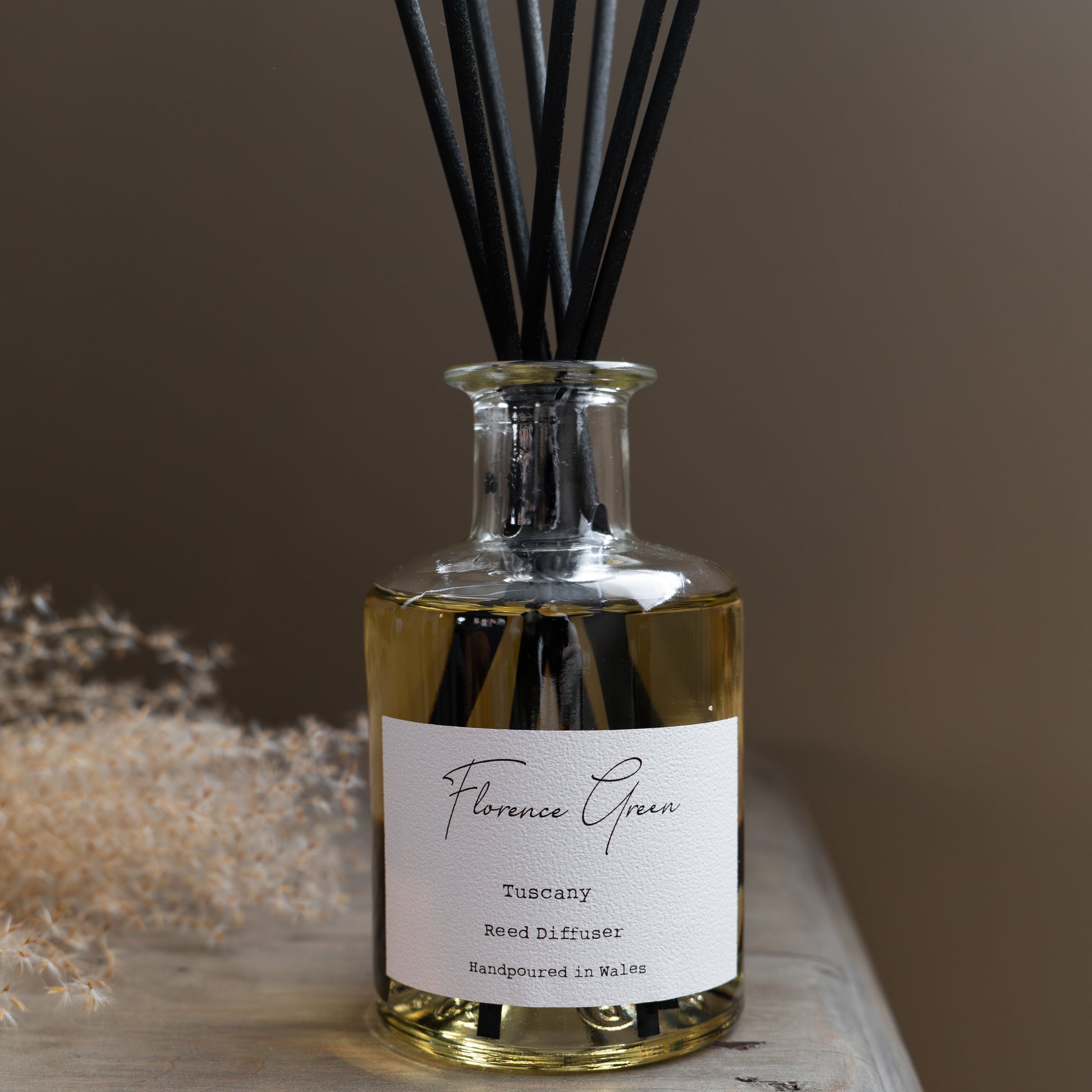 Reed diffuser bottle with black reeds on a wooden surface against a brown background