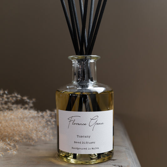 Reed diffuser bottle with black reeds on a wooden surface against a brown background
