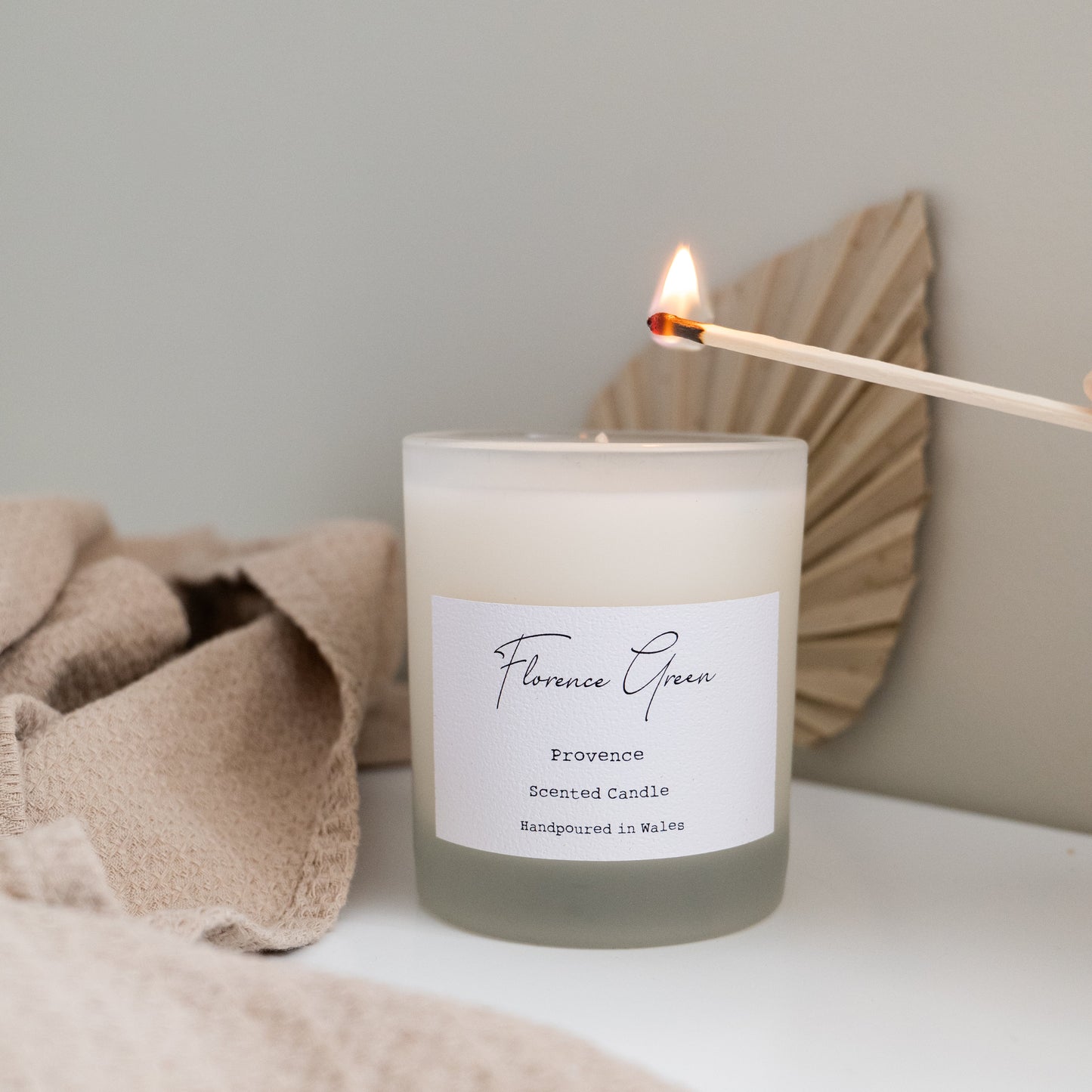 Candle with a label on a surface, surrounded by soft textures and neutral colors.