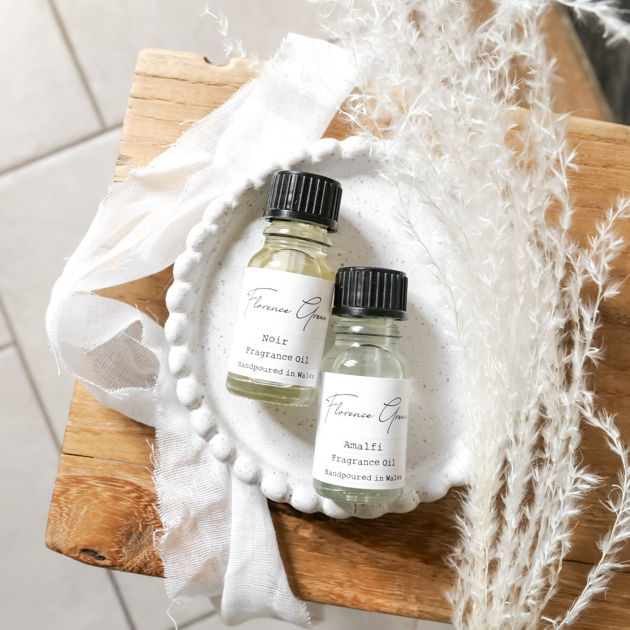 Two small bottles with black caps on a wooden surface with white fabric