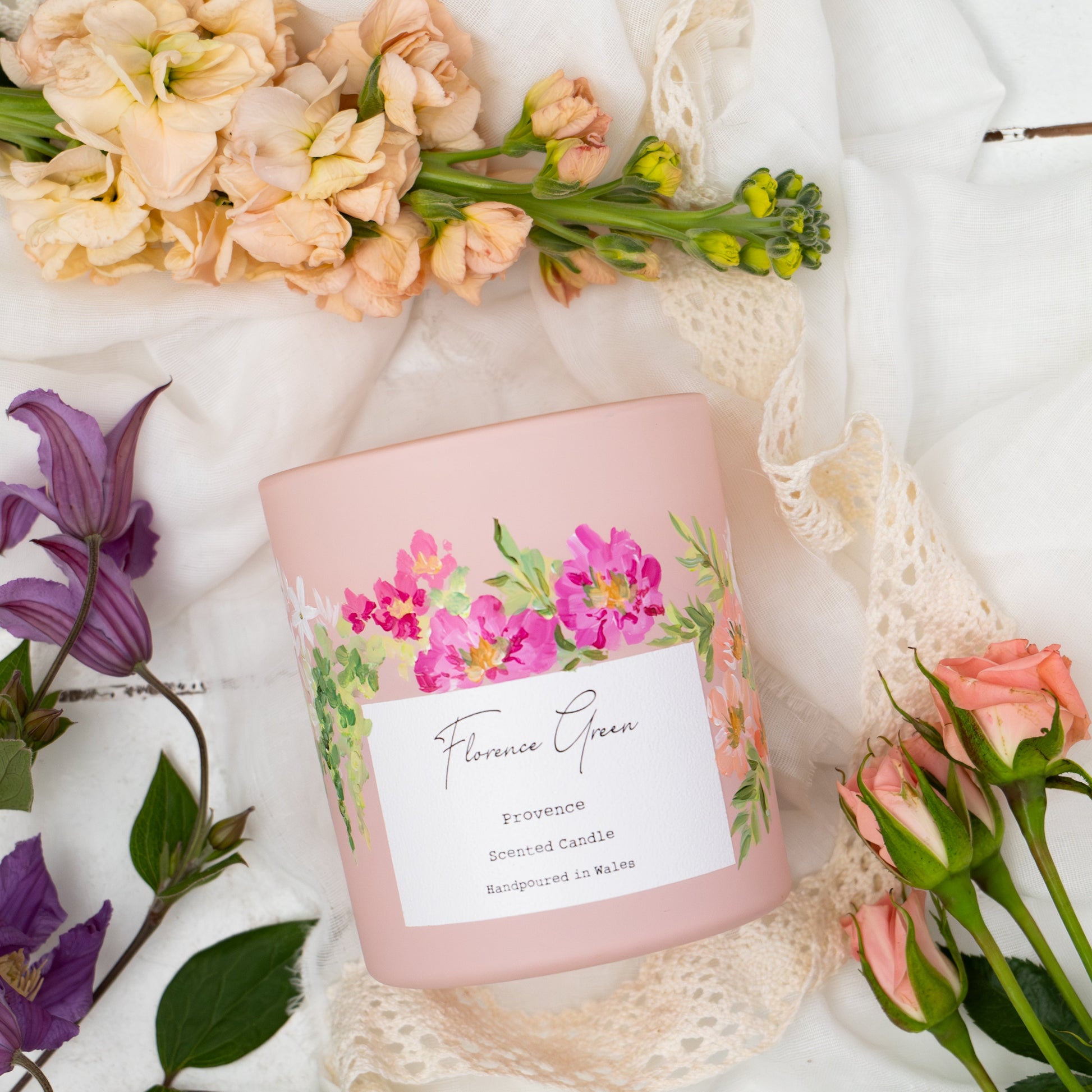 Pink candle with floral design and label on a white surface with flowers